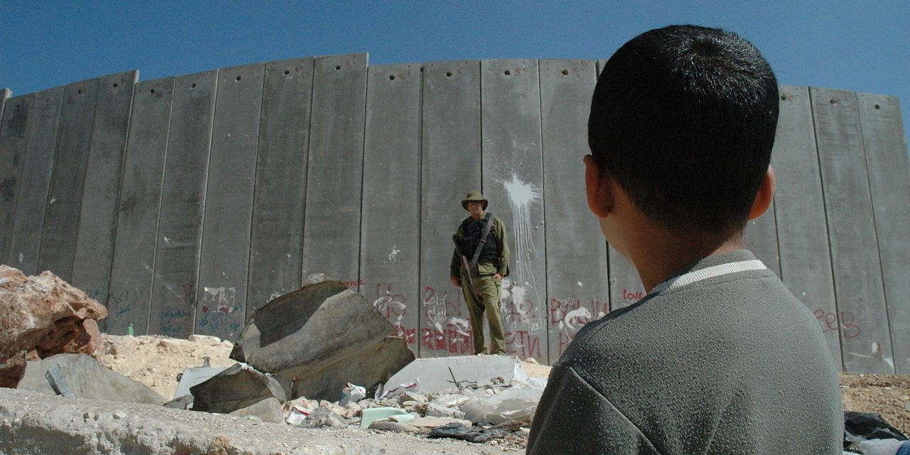 Un niño palestino mira a un soldado israelí junto al muro ilegal es West Bank, Palestina